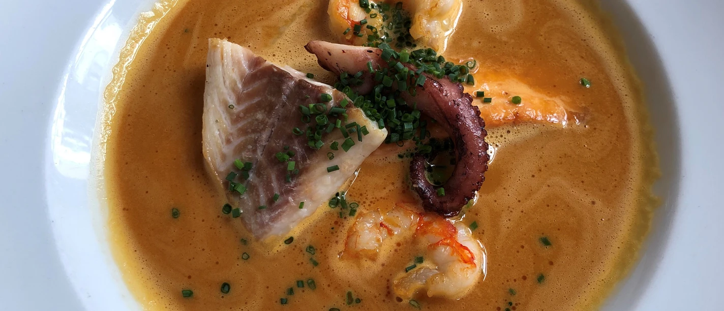 Een gouden vissoep met garnalen, stukjes vis en inktvisarmen, gegarneerd met verse bieslook.