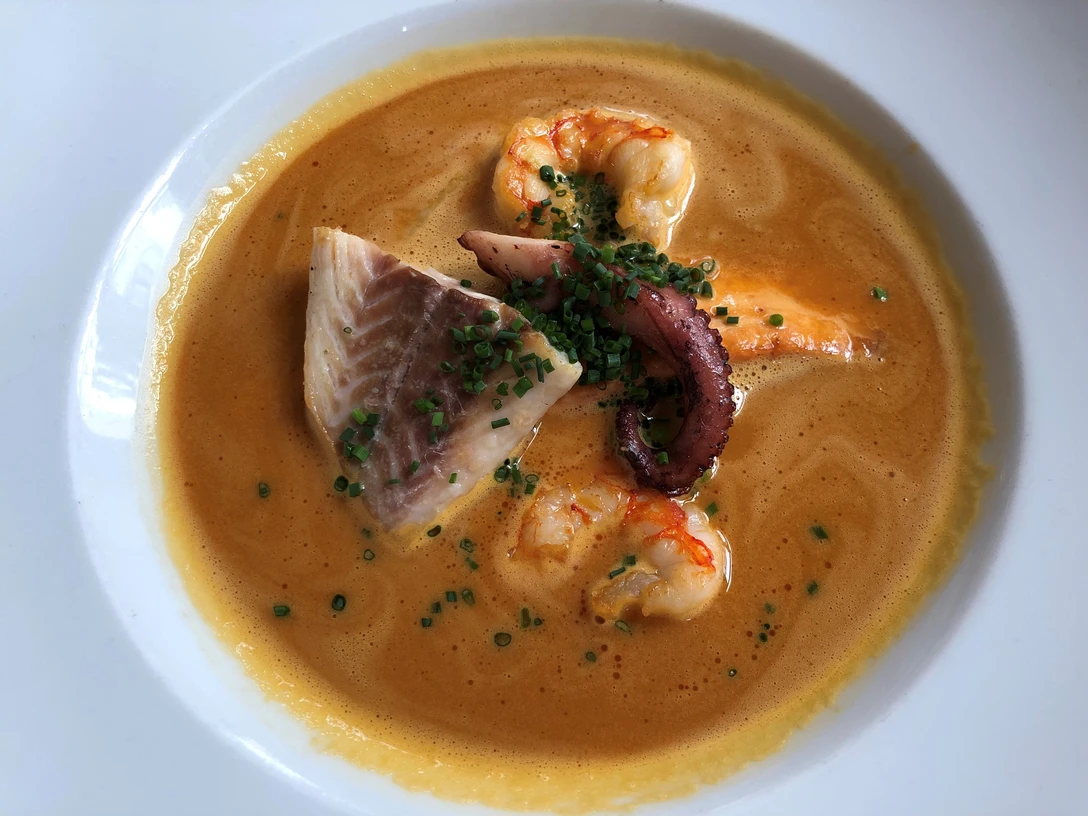 Fischsuppe Eine goldene Fischsuppe mit Garnelen, Fischstück und Tintenfischarme, garniert mit frischem Schnittlauch.