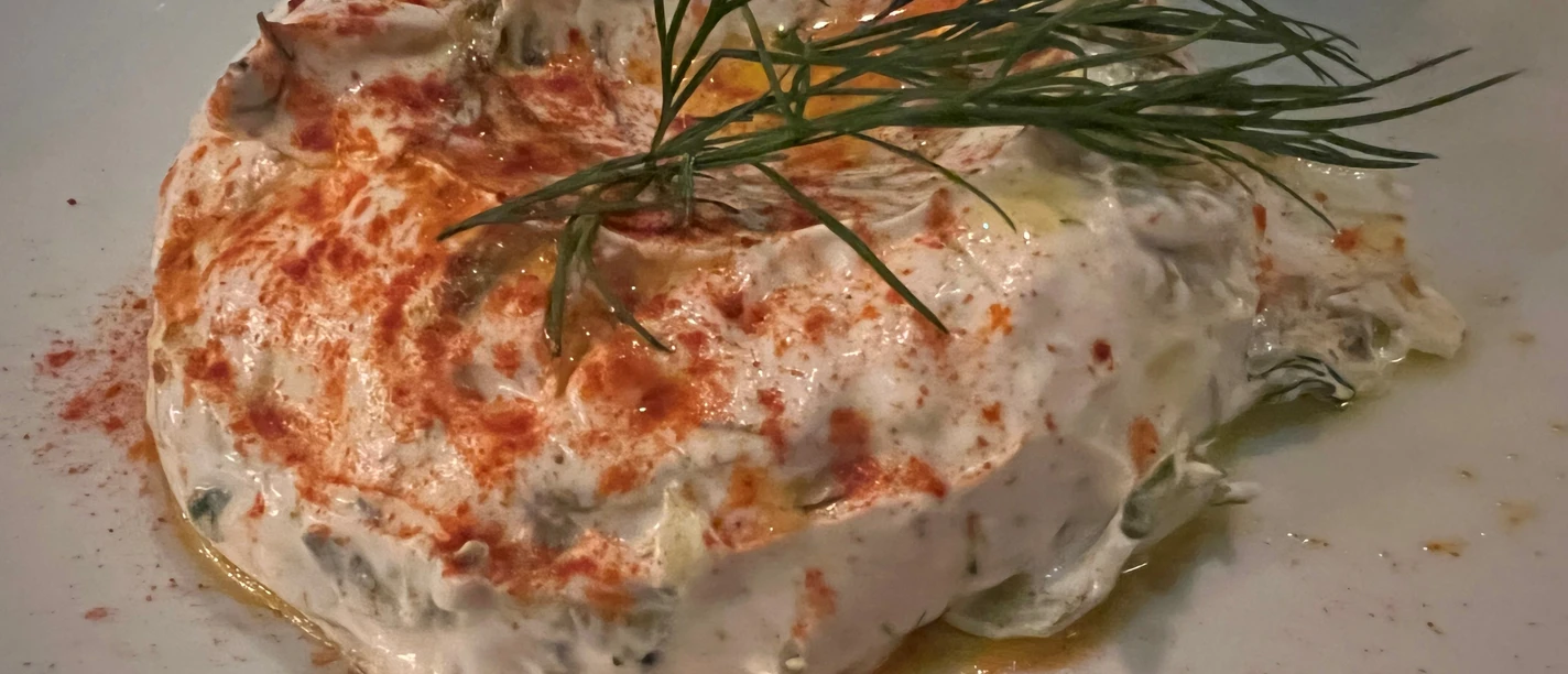 Griechisch Griechischer Joghurt-Dip auf einem weißen Teller, garniert mit Dill und leicht bestreutem Paprika.