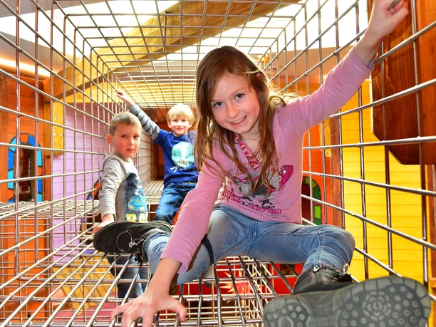 Indoorspielplatz Drei Kinder spielen fröhlich in einem Kletterkäfig eines Indoorspielplatzes.