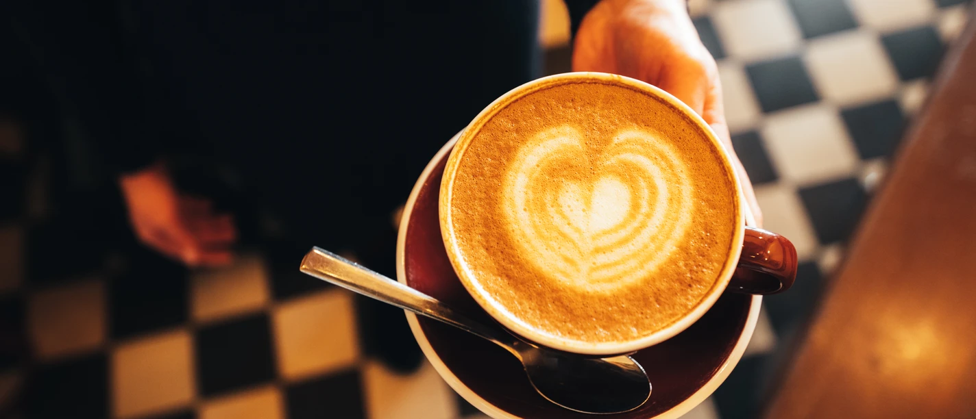 Une tasse de café avec de la mousse devant un sol carrelé noir et blanc, gastronomie, culture des cafés, cafés, plaisirs