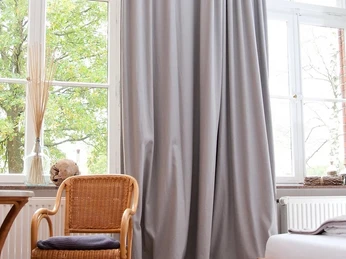 Gasthaus Rose - Hotel Alte Schule 2.jpg Helles Hotelzimmer mit großem Fenster, gemütlichem Bett, Holzmöbeln und einem Sessel vor grüner Aussicht.