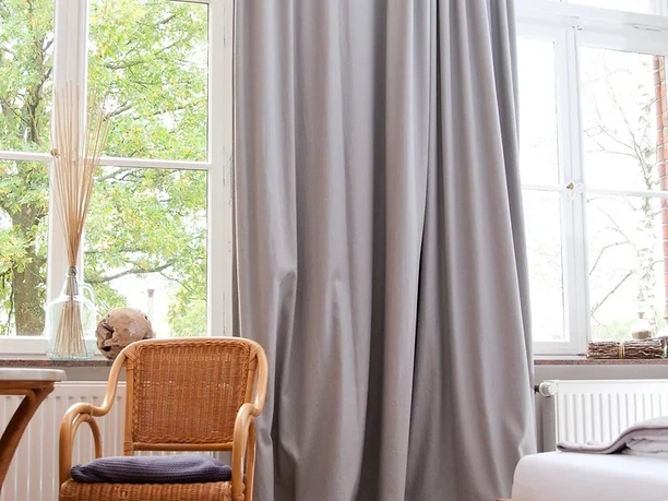 Gasthaus Rose - Hotel Alte Schule 2.jpg Helles Hotelzimmer mit großem Fenster, gemütlichem Bett, Holzmöbeln und einem Sessel vor grüner Aussicht.