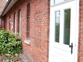 Gasthaus Rose - Hotel Alte Schule 1.jpg Ziegelbau neben gepflastertem Gehweg mit weißer Tür und Holzschild des Gasthauses Lechner Erfmeyer.