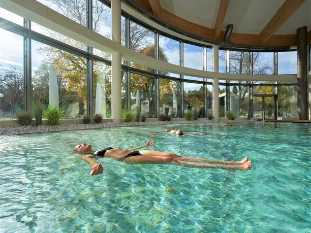 Relaxed person floats in a light-flooded spa with a wonderful view of the outdoor landscape.