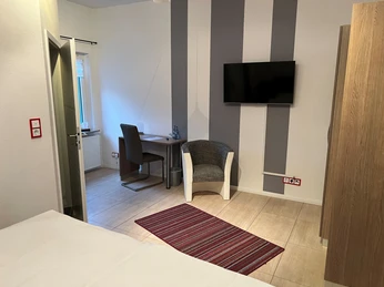 Steimkes Landhotel Zimmer Modern eingerichtetes Hotelzimmer mit einem Schreibtisch, Stuhl, Sessel und einem Flachbildfernseher.Modernly furnished hotel room with a desk, chair, armchair and a flat-screen TV.Moderne indrettet hotelværelse med skrivebord, stol, lænestol og fladskærms-tv.Modern ingerichte hotelkamer met een bureau, stoel, fauteuil en een flatscreentelevisie.