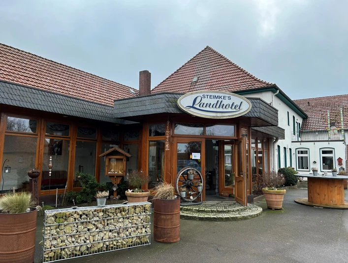 Steimkes Landhotel Eingang Eingang von Steimkes Landhotel mit runden Fenstern, Schindeldach und dezent begrünten Pflanzkübeln.Entrance to Steimke's country hotel with round windows, shingle roof and discreetly planted planters.Indgang til Steimkes landhotel med runde vinduer, spåntag og diskret beplantede krukker.Ingang van Steimke's plattelandshotel met ronde ramen, leien dak en discreet beplante plantenbakken.