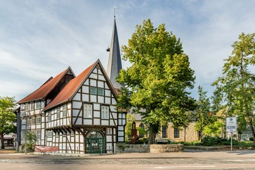 Fachwerkhaus und Kirche im Grünen, klare Architektur, idyllischer Ort, blauer Himmel, Sonnenschein.