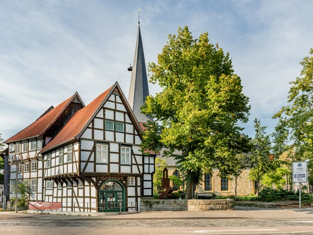 Fachwerkhaus und Kirche im Grünen, klare Architektur, idyllischer Ort, blauer Himmel, Sonnenschein.