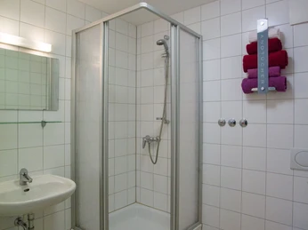 Alte Lübber Volksschule Barrierefreies Bad mit ebenerdiger Dusche, Handtuchhalter, Waschbecken und hellen Fliesen.