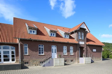 Lübber Volksschule Ehemalige Lübber Volksschule mit markantem roten Ziegeldach, historischen Backsteinwänden und drei Dachgauben.
