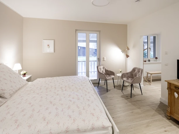 Doppelzimmer Helles Doppelzimmer mit großem Bett, zwei Sesseln, Holzfußboden und Terrassentür.