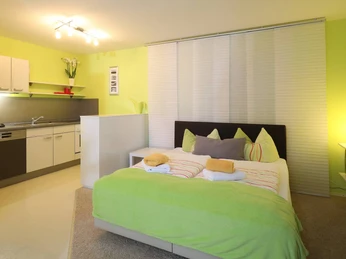 Ferienwohnung Hüllhorst Moderne Ferienwohnung mit offener Küche, Schlafbereich und warmem Licht in freundlichem Ambiente.