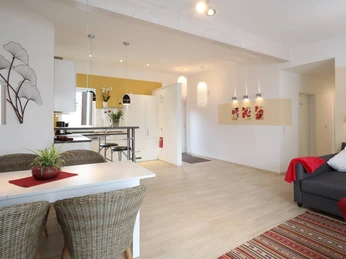 Ferienwohnung_Rubin.jpg Moderne Ferienwohnung mit heller Einrichtung, offener Küche, Essbereich, kunstvoller Wanddekoration.