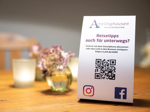 Aufsteller der Urlaubsregion Amelinghausen Aufsteller der Urlaubsregion Amelinghausen mit QR-Code für Reisetipps auf einem Holztisch.