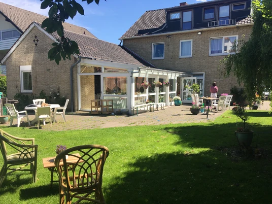Gästehaus Sonntag Eine grüne Wiese mit Rattanmöbeln vor einem einladenden Gästehaus mit Terrassenbereich und blühenden Pflanzen.