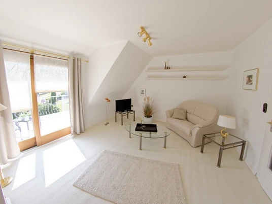 Wohnzimmer 1. Stock Helles Wohnzimmer im ersten Stock mit Sofa, Glastisch, kleinem Fernseher und Zugang zum Balkon.
