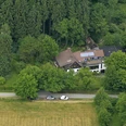Luftaufnahme eines Hauses am Waldrand mit Solarpanels auf dem Dach, umgeben von Bäumen und Feldern.