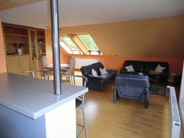 Am Huenenbrink-3.jpg Geräumiges Wohnzimmer mit Polstermöbeln, Esstisch und Dachfenstern. Schlichte Einrichtung in warmen Tönen.