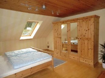 Am Huenenbrink-4.jpg Ein helles Schlafzimmer mit Holzdecke, Doppelbett, Kleiderschrank und einem Fenster mit Aussicht.