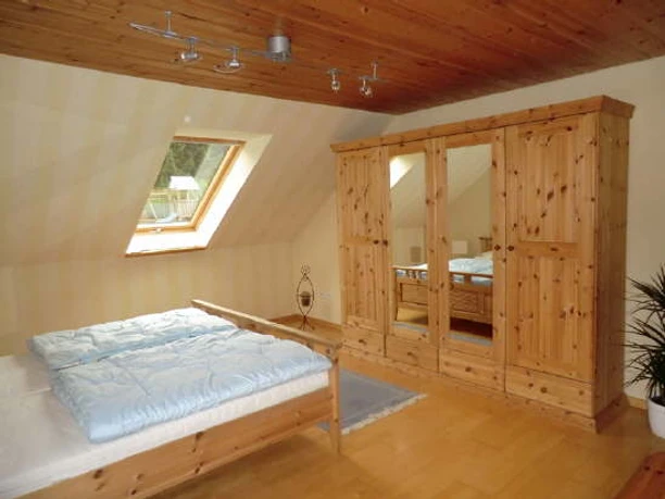 Am Huenenbrink-4.jpg Ein helles Schlafzimmer mit Holzdecke, Doppelbett, Kleiderschrank und einem Fenster mit Aussicht.