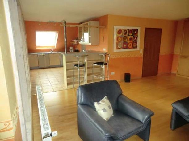 Am Huenenbrink-2.jpg Wohnzimmer mit offener Küche; Ledersessel im Vordergrund; orange Wand mit rundem Wandbild.