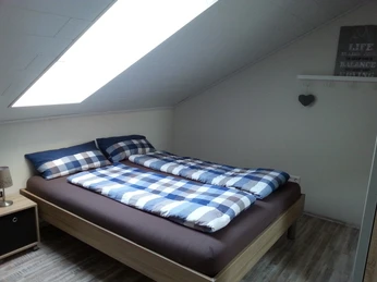 Gaesteappartement-Luebbecke-2.jpg Gemütliches Schlafzimmer mit Doppelbett, kariertem Bettzeug und Dachschräge, helle Atmosphäre.