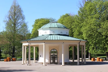 Brunnentempel im Historischen Kurpark Runder Pavillon mit Säulen und grüner Kuppel in einem grünen Kurpark, umgeben von Bäumen.