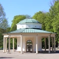 Brunnentempel im Historischen Kurpark Runder Pavillon mit Säulen und grüner Kuppel in einem grünen Kurpark, umgeben von Bäumen.