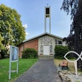 Ev. Kirche Evangelische Kirche mit hohem Glockenturm, gelegen in einer grünen Umgebung mit Parkbank und Gehweg.