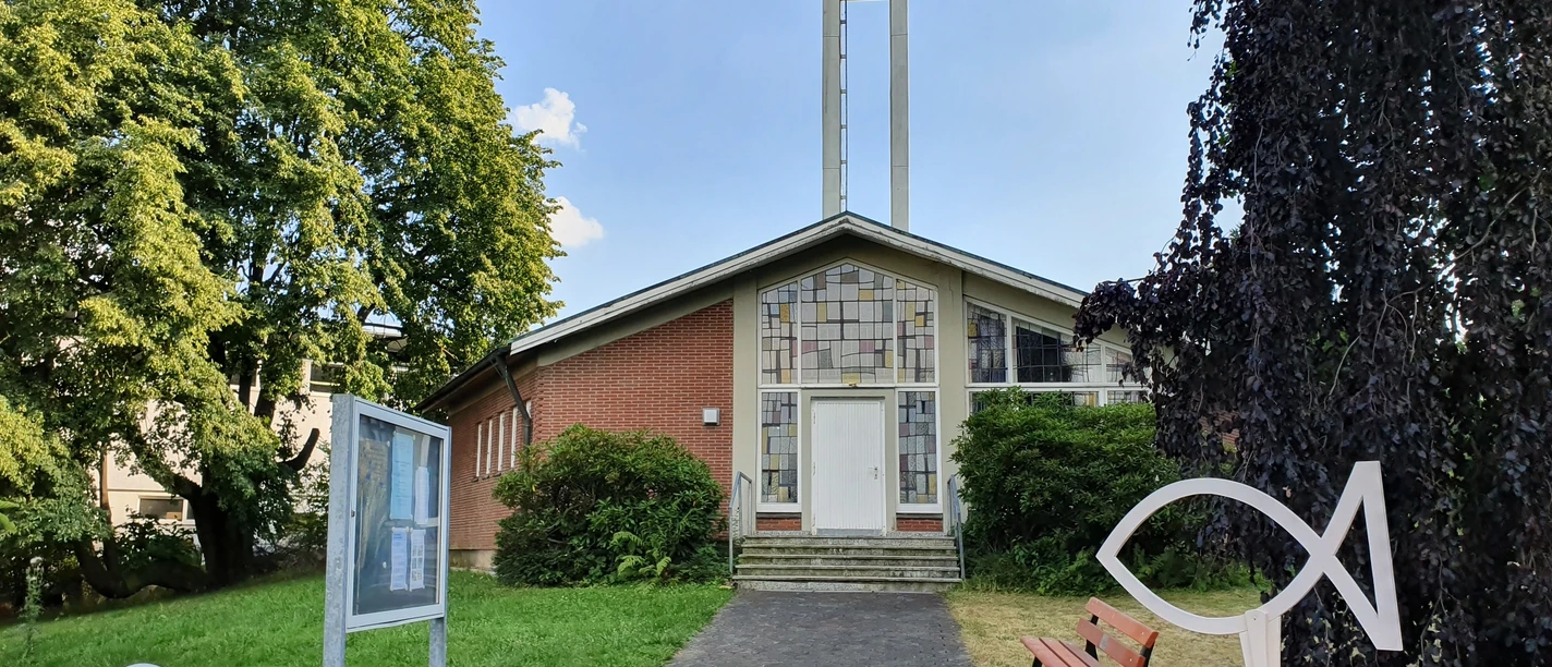 Ev. Kirche Evangelische Kirche mit hohem Glockenturm, gelegen in einer grünen Umgebung mit Parkbank und Gehweg.