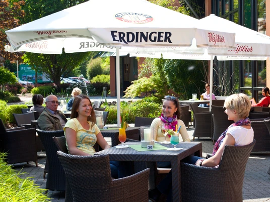 Lovina_groß-11-neu.jpg Menschen sitzen an einem Tisch im Freien unter einem großen weißen Sonnenschirm in einem Café.