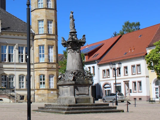 Franz Hausmann Denkmal Steinernes Denkmal mit Figuren auf einem Sockel, umgeben von historischen Gebäuden und Bäumen.