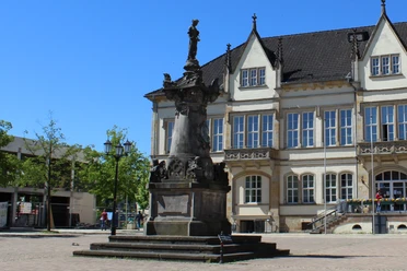 Das Franz Hausmann Denkmal steht vor einem historischen Gebäude auf einem gepflasterten Platz.
