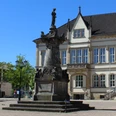 Das Franz Hausmann Denkmal steht vor einem historischen Gebäude auf einem gepflasterten Platz.