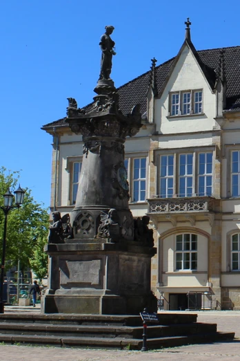 Das Franz Hausmann Denkmal steht vor einem historischen Gebäude auf einem gepflasterten Platz.