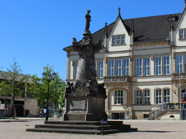 Das Franz Hausmann Denkmal steht vor einem historischen Gebäude auf einem gepflasterten Platz.