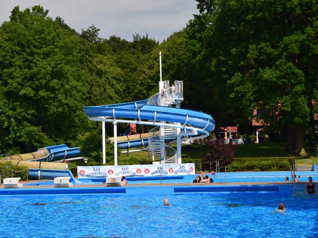 Freibad Bad Meinberg.png Das Bild zeigt ein Freibad mit einer großen Wasserrutsche, umgeben von grünen Bäumen und Schwimmern.