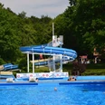 Freibad Bad Meinberg.png Das Bild zeigt ein Freibad mit einer großen Wasserrutsche, umgeben von grünen Bäumen und Schwimmern.