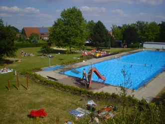Freibad_Belle.jpg Freibad mit großem Schwimmbecken, Rutsche, Liegewiese und vielen Besuchern an einem sonnigen Tag.
