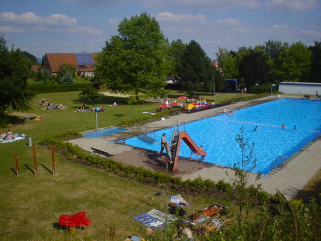 Freibad_Belle.jpg Freibad mit großem Schwimmbecken, Rutsche, Liegewiese und vielen Besuchern an einem sonnigen Tag.
