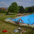 Freibad_Belle.jpg Freibad mit großem Schwimmbecken, Rutsche, Liegewiese und vielen Besuchern an einem sonnigen Tag.