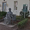 Fürstin Pauline Bronzestatue der Fürstin Pauline mit Buch in der Hand, vor einem Gebäude mit Schautafel, umgeben von Büschen.