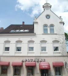 Ein weißes, zweistöckiges Gebäude mit rotem Dach und mehreren Fenstern, das als Apotheke dient.