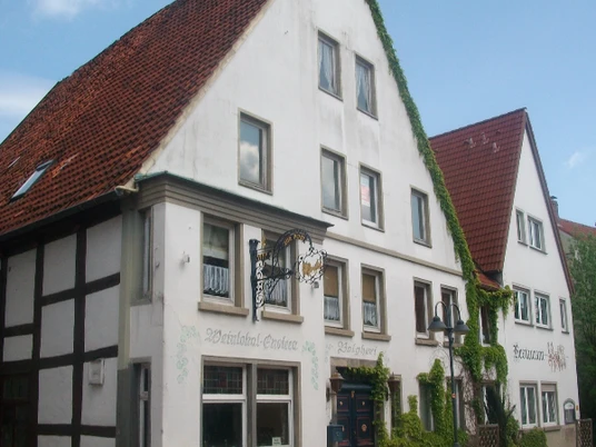 Fachwerkhaus mit roten Ziegeldächern, begrüntem Fassadenbereich und angrenzendem Gebäude.