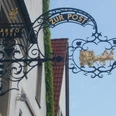 Schwarzes, kunstvoll geschmiedetes Wirtshausschild "Zur Post" mit golderner Postkutsche und Pferden.