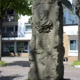 Kaiser-Wilhelm-Denkmal.png Steinernes Denkmal mit Kaiser Wilhelm-Büste, umgeben von Stadtgebäuden und Bäumen.