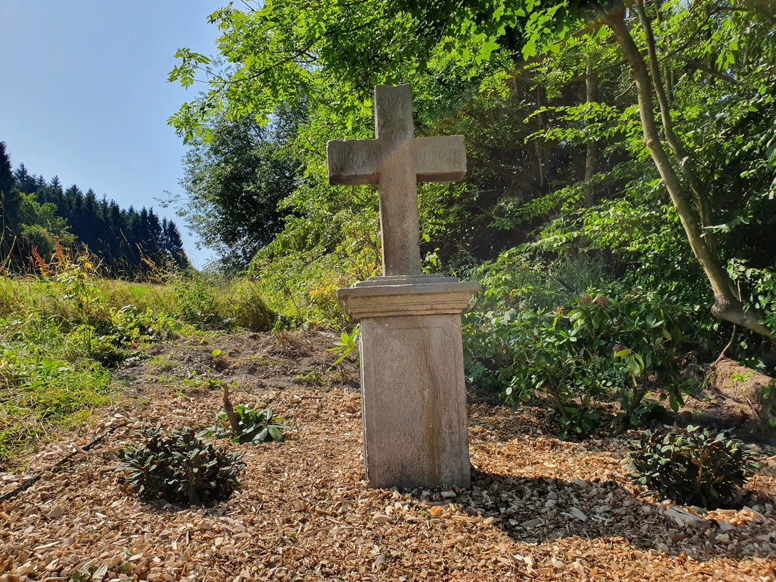 Kreuz am Bickelberg Steinernes Kreuz auf einer Anhöhe umgeben von Bäumen und Grün, mit Lichtspiel der Sonne.