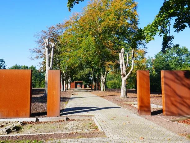 12.03.2022_Exkursion_Gedenkstätte Esterwegen.jpg Gedenkstätte mit rostfarbenen Stahltafeln und Baumallee unter blauem Himmel in Esterwegen.