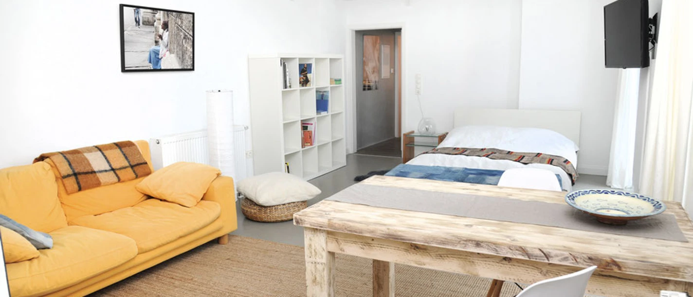 Ferienwohnung Sieveking u. Grünert Helles Wohn- und Schlafzimmer mit gelbem Sofa, Holztisch und Doppelbett in einer modernen Ferienwohnung.